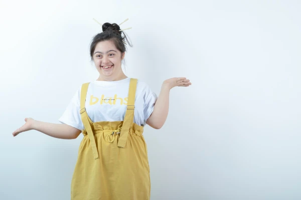 Foto de criança especial branca sorrindo com blusa branca e macacão amarelo.